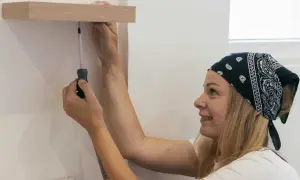 Une femme souriante utilise un tournevis pour fixer deux meubles entre eux sans percer.