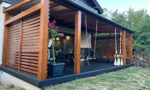 Drewniany taras na kostce brukowej z huśtawkami i meblami ogrodowymi.