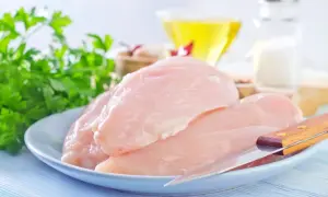Surowe piersi kurczaka na talerzu z natką pietruszki, oliwą i solniczką w tle.