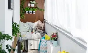 Przytulny balkon w bloku z wielkiej płyty, z wygodną kanapą, ziołami na półkach i kwiatami.