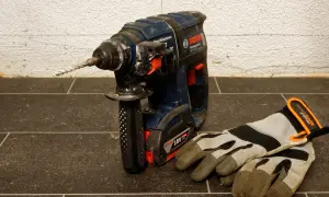 Mocna wiertarka udarowa Bosch z zamontowanym wiertłem i rękawicami roboczymi obok. Dowiedz się, jak wyjąć wiertło z wiertarki.