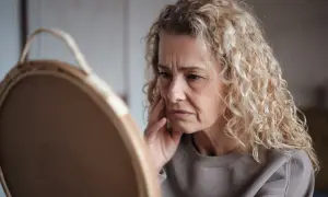 Besorgte Frau betrachtet sich im Spiegel. Sie fragt sich, ob Kollagen bei Haarausfall hilft.
