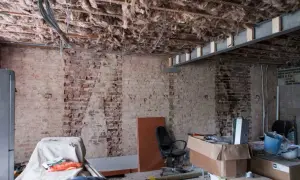 Pågår renovering av funkishus. Synligt bjälklag med isolering och tegelväggar. Material och verktyg ligger utspridda.