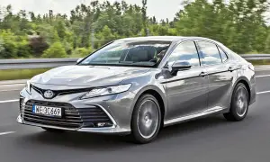 Srebrna Toyota Camry 2023 jedzie po drodze, otoczona zielenią drzew.