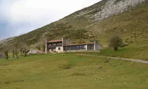 Edificio de piedra con tejado rojo en ladera verde. Un lugar donde se puede comer en los Lagos de Covadonga, con un camino y un árbol solitario.