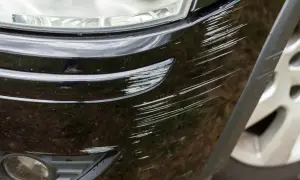 Porysowany czarny zderzak, potencjalne przyczyny trzeszczenia zderzaka podczas jazdy po nierównościach.