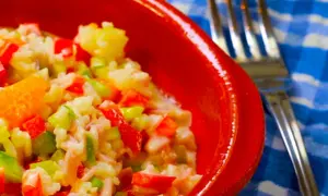 Omas Reissalat, ein bunter Mix aus Reis, Paprika, Sellerie und Mandarine, serviert in einer roten Schüssel.