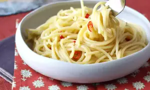 En skål med spaghetti aglio olio e peperoncino, där en gaffel lyfter upp en del av den oljiga pastan med små röda chilistrimlor.