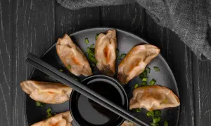 Złociste pierogi z kimchi, posypane szczypiorkiem, czekają na zanurzenie w sosie.