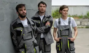 Trzech pracowników w szarych kombinezonach z neonowymi akcentami. Polski producent odzieży roboczej prezentuje nowoczesne ubrania.