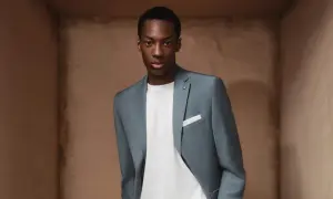Junger Mann in einem stilvollen hellblauen Anzug. Die Anzugfarbe passt perfekt zu seinem weißen T-Shirt und dem neutralen Hintergrund.