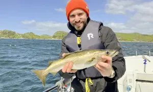 Glücklicher Angler mit frisch gefangenem Fisch vor der Küste von Farsund. Ein perfekter Tag für Angeln Hotspots!