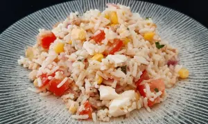 Une généreuse portion de salade de riz thon, garnie de dés de tomates, de maïs et d'œufs durs, sur une assiette texturée.