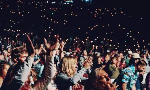 Tłum ludzi na koncercie, trzymający w górze telefony z zapalonymi latarkami.