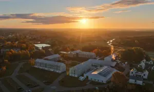 Zachód słońca nad nowoczesnym kompleksem budynków, przypominającym spokojny folwark lochów, otoczonym jesienną przyrodą i rzeką.