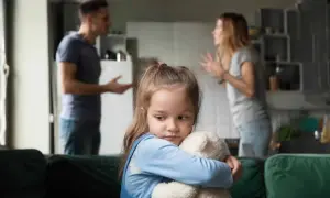 Smutna dziewczynka tuli misia, podczas gdy rodzice kłócą się w tle. Temat: pozbawienie praw rodzicielskich a alimenty.