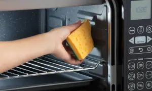 Mano che pulisce l'interno di un fornetto elettrico con una spugna gialla. Guida su come pulire il fornetto elettrico.