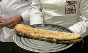 Una paposcia pugliese, ripiena e dorata, servita su un piatto grigio. Indossano giacche con stemmi dell'Associazione Pizzaioli Garganici.