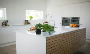 Nowoczesna kuchnia z wyspą z blatem z **korianu**. Na blacie zioła w doniczkach, chleb i owoce.