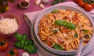 Ein Teller Spaghetti Napoli mit Tomatensauce, Basilikum und Parmesan. Daneben frische Tomaten, Knoblauch und Kräuter.