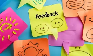 Kolorowe karteczki z rysunkami i napisem "feedback". Jedna pokazuje smutną i wesołą buźkę, symbolizując konstruktywny feedback.