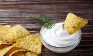 Nachos z gęstym, białym sosem śmietanowym i gałązką koperku na drewnianym tle.