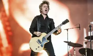 Billie Joe Armstrong z Green Day Saviors śpiewa i gra na gitarze na scenie, z perkusją w tle.