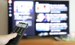 Dłoń z pilotem przed ekranem telewizora, na którym widać menu aplikacji. Dowiedz się, jak ściągnąć aplikację na telewizor.