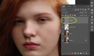 Primo piano di un volto femminile con capelli rossi. Pannello Livelli di Photoshop aperto, evidenziato il livello "texture" per la separazione delle frequenze.