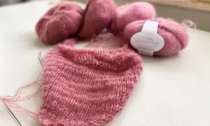 Zartrosa Mohair-Garn liegt neben einem Strickprojekt. Die feinen Fasern des Mohairs fusseln leicht und versprechen ein luftiges, weiches Ergebnis.