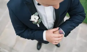 Elegancka butonierka dla pana młodego i świadka, ozdobiona białymi kwiatami i zielonymi liśćmi, dodaje szyku granatowemu garniturowi.