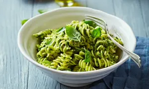 Eine Schüssel Fusilli-Nudeln mit grünem Pesto und frischem Basilikum, garniert mit einer Gabel.