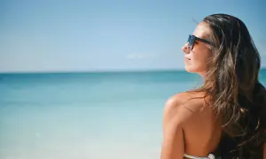 Kobieta w okularach przeciwsłonecznych patrzy na morze. Marzy o urlopie bezpłatnym do 30 dni, by odpocząć na plaży.