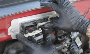 Manos enguantadas trabajan en la caja de fusibles, conectando un componente que podría ser el PCM, el cerebro del vehículo.