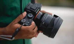 Dłonie trzymają aparat Sony z obiektywem Sigma. Widoczna jest skala ogniskowa obiektywu, wskazująca na jego możliwości.