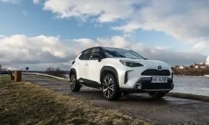 Biały Toyota Cross Yaris zaparkowany nad rzeką, z chmurami na niebie.