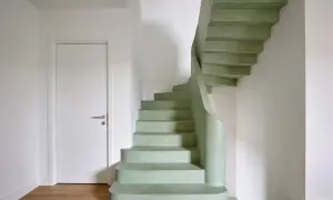 Escaleras curvas de microcemento en tono verde menta, con una puerta blanca y suelo de madera.