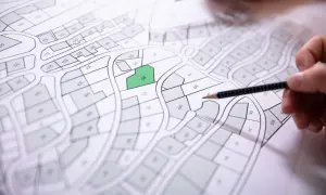 Des parcelles sont dessinées sur des matrices cadastrales, une est mise en évidence en vert. Des mains tiennent des crayons pour étudier le plan.