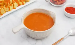 Un cuenco de cremosa salsa brava, lista para acompañar unas patatas. En el fondo, pimentón y guindillas secas.