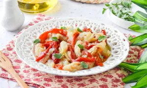 Deliciosa ensalada de bacalao con pimientos rojos asados y hierbas frescas, servida en un plato blanco decorado.