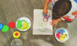 Niño pequeño creando arte con pintura de dedos. Lienzo con círculos de colores y recipientes de pintura.