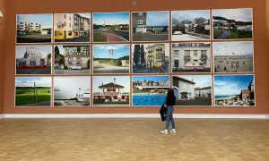 Mostra di fotografie di Raymond Depardon: paesaggi urbani, rurali e marittimi, con una donna che osserva le opere.