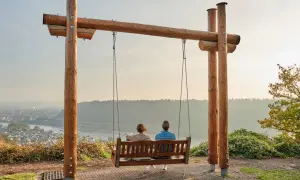 Zwei Personen auf einer Schaukel genießen den Ausblick auf eine Stadt am Fluss. Ein magischer Ort in Rheinland-Pfalz, der zum Verweilen einlädt.
