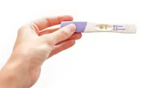 Dłoń trzyma test ciążowy z dwoma kreskami, wskazującymi na pozytywny wynik. Test wykrywa hormon hcg.