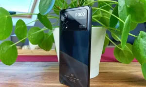 Czarny smartfon POCO X4 z potrójnym aparatem 108MP, otoczony zielonymi liśćmi rośliny.