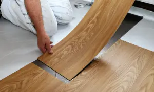 Hand verlegt Holzoptik PVC Boden. Ein Mann kniet und legt eine Diele auf den Untergrund.