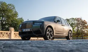 Elegancki Rolls-Royce Cullinan na kamienistej drodze, z grillem i charakterystyczną figurką na masce.