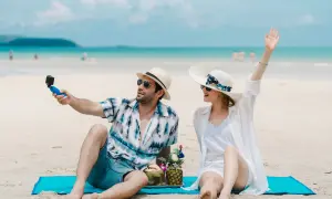 Para na plaży nagrywa filmik kamerką, a jego partnerka macha do obiektywu. Idealne wczasy pod gruszą!