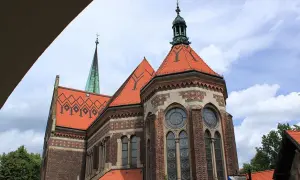 Suchanino kościół z zieloną wieżą i ceglaną fasadą, ozdobiony czerwonymi dachami i ozdobnymi oknami.