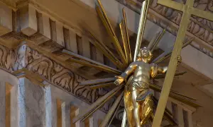 Złoty posąg Chrystusa z krzyżem, otoczony promieniami. Jego postawa mówi: "Jestem który jestem".